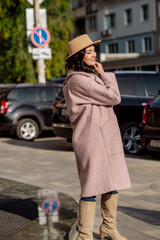 beautiful caucasian brunette woman in a stylish outfit walking down the street in the offseason in a coat and hat
