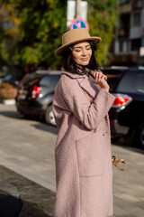 beautiful caucasian brunette woman in a stylish outfit walking down the street in the offseason in a coat and hat
