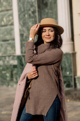 beautiful caucasian brunette woman in a stylish outfit walking down the street in the offseason in a coat and hat
