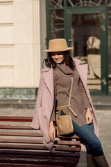 beautiful caucasian brunette woman in a stylish outfit walking down the street in the offseason in a coat and hat
