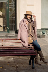 beautiful caucasian brunette woman in a stylish outfit walking down the street in the offseason in a coat and hat
