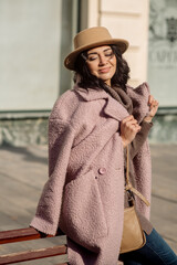 beautiful caucasian brunette woman in a stylish outfit walking down the street in the offseason in a coat and hat
