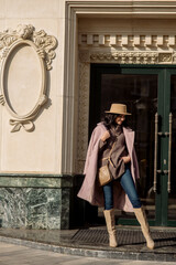 beautiful caucasian brunette woman in a stylish outfit walking down the street in the offseason in a coat and hat
