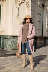 beautiful caucasian brunette woman in a stylish outfit walking down the street in the offseason in a coat and hat

