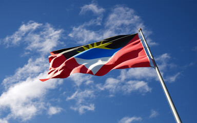 Beautiful national state flag of Antigua and Barbuda fluttering at sky background. Low angle close-up flag 3D artwork.