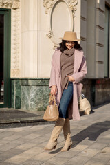 beautiful caucasian brunette woman in a stylish outfit walking down the street in the offseason in a coat and hat
