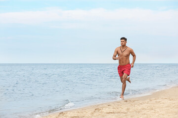 Fototapeta na wymiar Handsome male lifeguard running on sandy beach