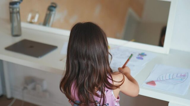 Little girl coloring different types of leaves on a paper sheet with a pen