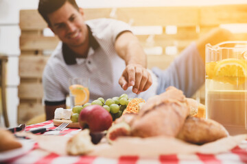 Obraz na płótnie Canvas Man with tasty food and drink imitating picnic at home