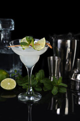  Tequila, Citrus liquor, lime juice - this is a Margarita cocktail. A  of lime with a sprig of mint decorates a glass. Dark  moody food