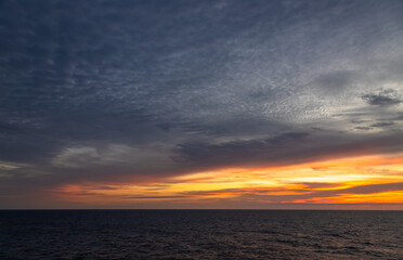 Naklejka na ściany i meble Sunset and dramatic set of clouds drifting over the tropical waters of the Caribbean Sea are lit by the last moments of daylight.