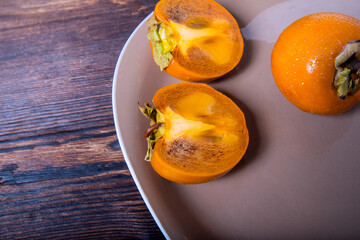 Persimmon cut in half and whole persimmon on a plate on a wooden table, close-up, copy space