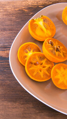 Persimmon cut into slices and halves of persimmon on a plate on a wooden table, close-up, copy space