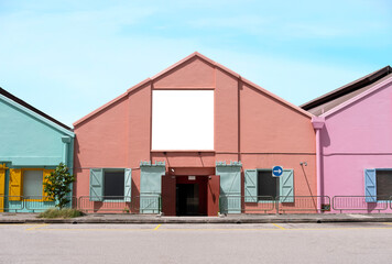 Fototapeta premium Billboard mock up in suburb background with clear sky. Template of an empty information billboard on colorful buildings near roadside with clear road, Mock-up of banner placeholder and poster.