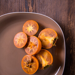 Persimmon sliced in half with water drops on a plate on a wooden table top view close-up, copy space