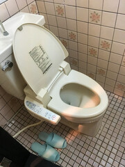 TOKYO, JAPAN - APRIL 3, 2018: Japanese toilet with remote control, slippers next to it. Small...