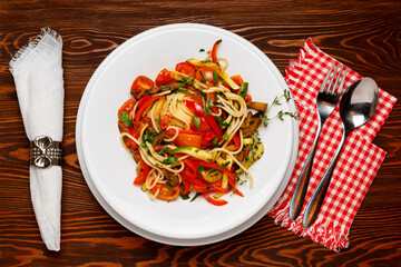 Vegetarian pasta with paprika and tomatoes on a white plate on a dark wooden table, fork and spoon