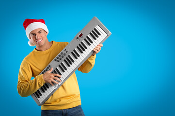 Man in Santa hat playing synthesizer on light blue background, space for text. Christmas music