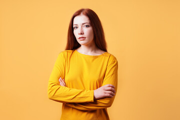 colorful studio portrait of confident young woman with her arms folded - yellow orange color background with copy space