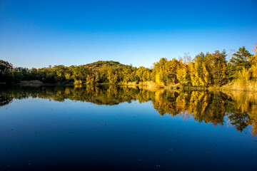 A beautiful little lake called Schnepfensee in Germany at a sunny day in Autumn with a colorful forest reflecting in the water.