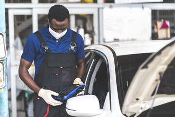 African American black people. Professional car mechanic repair service and checking car engine by Diagnostics Software computer. People wearing medical face mask against the corona virus covid 19.