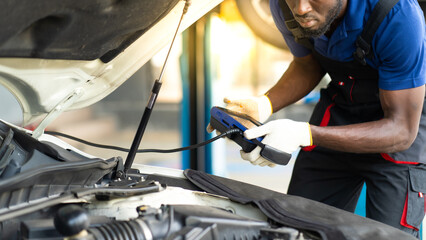 Professional car mechanic repair service and checking car engine by Diagnostics Software computer. Expertise mechanic working in automobile repair garage.