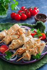 Chicken skewers on wooden skewers with vegetables on a ceramic plate, selective focus