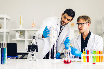 Fototapeta premium Professional two scientist man research and working doing a chemical experiment while making analyzing and mixing liquid in test tube.Young science man dropping sample chemical on glass at laboratory