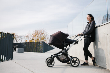 Mother with a pram or stroller on modern city streets walking and relaxing in autumn