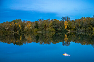 A beautiful little lake called Schnepfensee in Germany at a sunny day in Autumn with a colorful forest reflecting in the water.