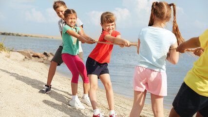 Cute little children playing tug of war game near river on sunny day