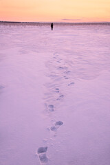 Footprints of a departing man in the snow in a field at sunset