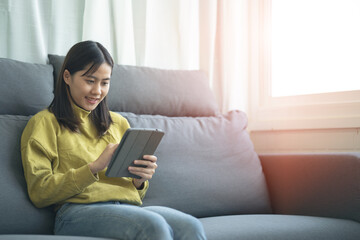 Fototapeta premium An Asian woman sitting on a tablet on a sofa