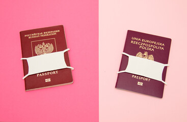 Russian passport and Poland passport with paper masks on pink background