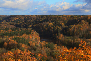 autumn in the forest on the hills with a river and blue sky with clouds 
