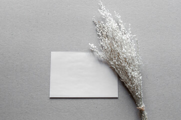 Bridal stationery still life. Closeup of blank business card mock-up near bouquet of white dried flowers on grey background. Flat lay, top view. Wedding concept