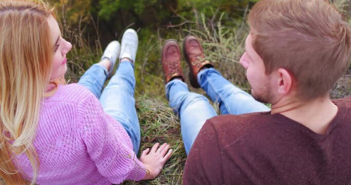 Young couple sits on cliff mountain on walk through autumn forest. Sitting on grass they look at each other and have fun. High quality 4k footage