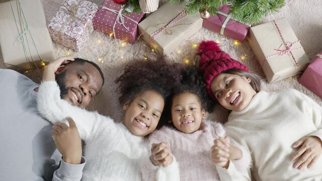 Portrait top view happy black parents and little cute children african american family having fun lying down on floor carpet at home or apartment looking at camera smile and laugh together.