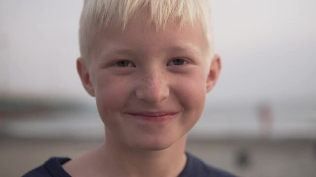 Close-up of the face of the happy boy blond with freckles against the background of the washed-up sea and beach.