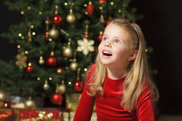 ein kleines mädchen schaut erwartungsvoll zur seite vor dem weihnachtsbaum, textfreiraum