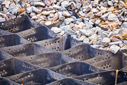 Cellular confinement system - plastic black honeycomb frame filled with small natural stones closeup. Used in construction for erosion control, soil stabilization on flat ground and steep slopes