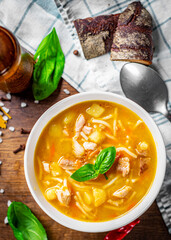 Chicken soup with noodles and vegetables in white bowl on wooden table background