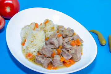 Hot dish of pilaf with meat and rice. White plate, blue background top view