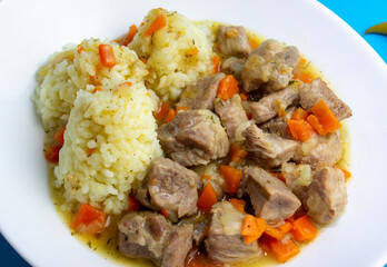 Hot dish of pilaf with meat and rice. White plate, blue background top view