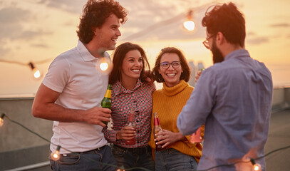 Cheerful friends with beer enjoying outdoor party on rooftop