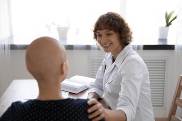 Close up rear view doctor supporting hairless woman at meeting, touching shoulder, patient...