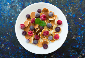 Plate with mini pancakes and berries on a dark blue background. Flat lay.