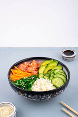 Poke bowl, traditional Hawaiian and Japanise raw fish salad, from seaweed, rice, salmon, cucumber and avocado. and sesame seeds on a teal blue and white background. An overhead, Copy space.