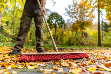 Mit großem Besen Blätter im Herbst zusammen fegen