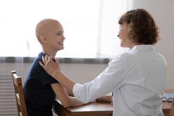 Rear view smiling doctor touching hairless female patient shoulder at meeting, supporting,...